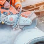 Construction worker cutting concrete pipe for drainage using a cut off saw Cutting concrete with a diamond blade creating cloud of silica dust
